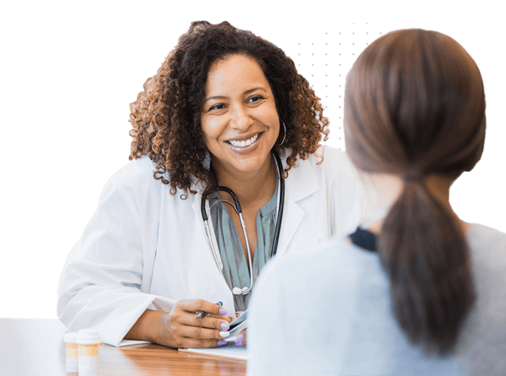 Smiling female doctor with a stethoscope around her neck talking to a female patient across the desk